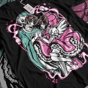May include: A black t-shirt featuring a graphic print of two anime characters. The characters are a boy with green hair and a girl with pink hair. The boy is wearing a green outfit and the girl is wearing a pink dress. The background is a swirl of pink and white.