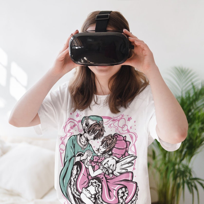 May include: A white t-shirt featuring a graphic print of two anime characters. The characters are a boy and a girl, holding hands. The boy is wearing a green shirt and a hat, and the girl is wearing a pink dress. The background of the graphic is a pink and white swirl.