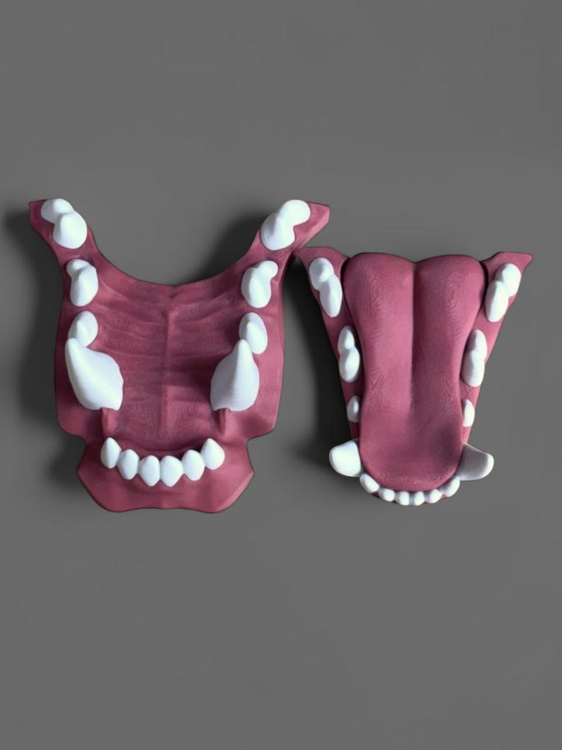 May include: Two separate 3D-printed jaw models featuring a dark pink gum and tongue texture with sharp, white, pointed teeth. The left piece shows an open upper jaw structure, while the right piece displays a lower jaw with a prominent central tongue.