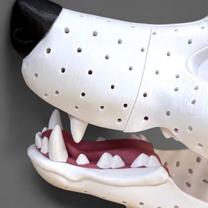 May include: A white animal head sculpture featuring a black nose, a perforated surface texture, and an open mouth revealing a red tongue and white teeth. The structure is composed of multiple segments joined together, showing a detailed canine-like jaw.