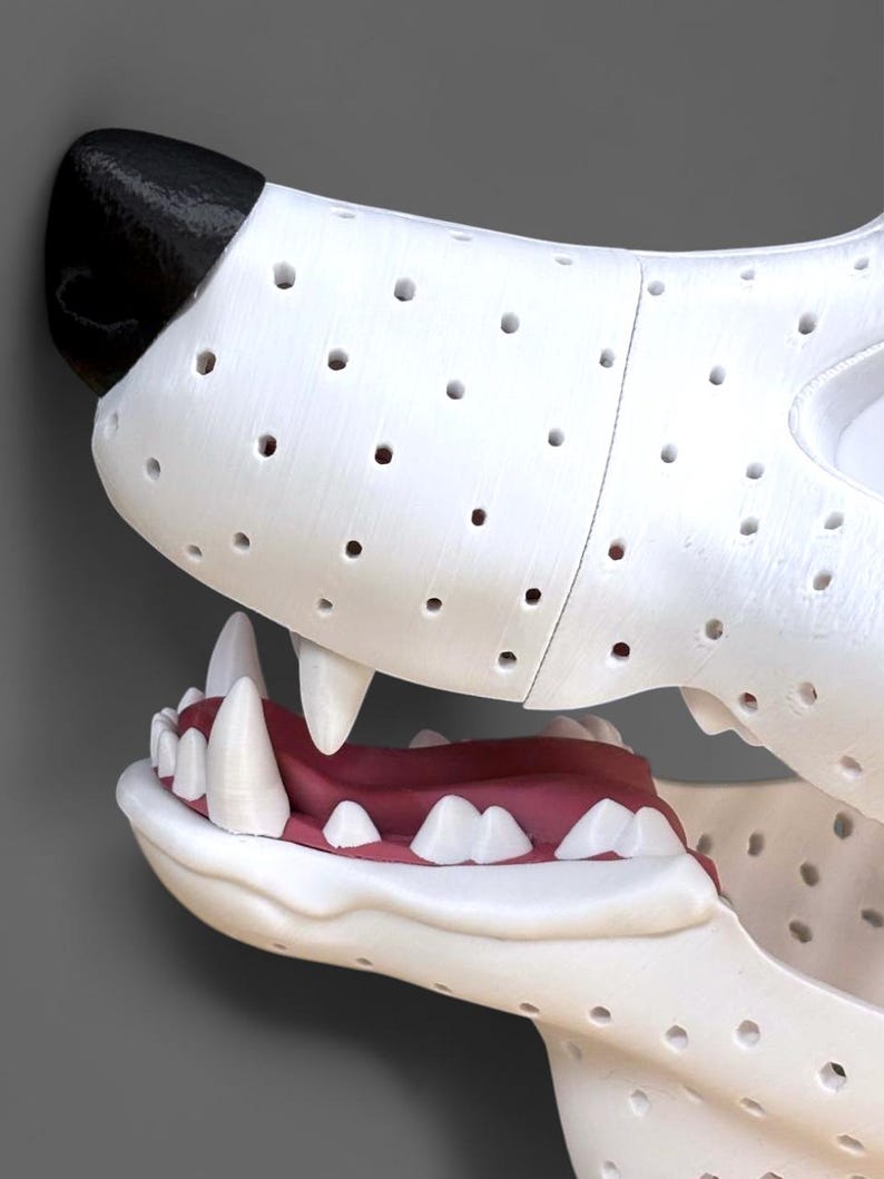 May include: A white animal head sculpture featuring a black nose, a perforated surface texture, and an open mouth revealing a red tongue and white teeth. The structure is composed of multiple segments joined together, showing a detailed canine-like jaw.