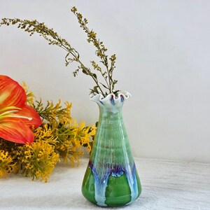K&ouml;nnte beinhalten: Eine Keramikvase mit einem ausgestellten, ger&uuml;schten Rand und einem konischen K&ouml;rper. Die Glasur zeigt einen Verlauf von Hellgr&uuml;n oben, der in ein dunkelviolettes und blaues Tropfmuster auf einer leuchtend gr&uuml;nen Basis &uuml;bergeht, mit braunen Stielen.