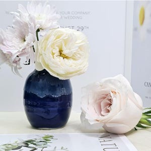 Puede incluir: Un jarr&oacute;n de cer&aacute;mica azul con un glaseado blanco en el borde superior contiene un ramo de rosas blancas y rosas y crisantemos blancos.