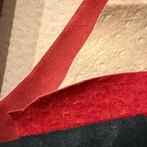 Peut inclure: Gros plan sur un tapis textur&eacute; avec un motif compos&eacute; de sections rouges, beiges et bleu fonc&eacute;. La section rouge forme une bande diagonale sur le fond beige, avec une section bleu fonc&eacute; en bas.