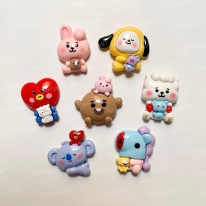 May include: A selection of colourful cartoon character charms. The charms feature various designs, including a pink bunny holding a cup, a yellow character with black ears, and a red heart with a face. These charms are likely for crafting or jewellery making.