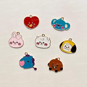 Könnte beinhalten: Eine Sammlung bunter Emaille-Anhänger mit Cartoon-Charakter-Designs. Die Anhänger umfassen ein rotes Herz, einen blauen Koala, ein rosa Kaninchen, ein weißes Schaf, einen gelben Charakter, ein blaues Pferd und einen braunen Bären. Jeder Anhänger hat eine goldfarbene Schlaufe.