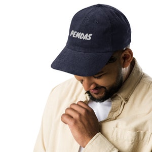 May include: A navy blue corduroy baseball cap with white embroidered text that reads "PEMDAS".