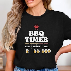 May include: Black t-shirt with a white graphic of a grill and the text "BBQ TIMER". The graphic also includes a scale with the words "Rare", "Medium", and "Well" and beer mugs to indicate the level of doneness.
