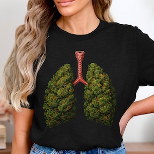 Könnte beinhalten: Schwarzes T-Shirt mit einer Grafik von Lungen, die aus grünen Cannabisblüten gebildet werden und durch eine rote Luftröhre verbunden sind. Das Design ist mittig platziert. Das T-Shirt wird getragen.