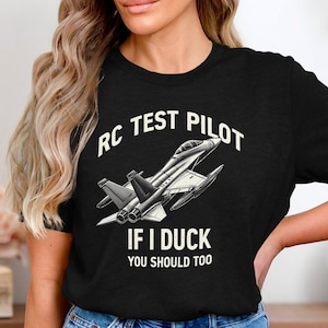May include: Black t-shirt with a white graphic of a jet plane and the text "RC Test Pilot If I Duck You Should Too".