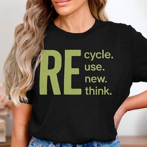 Könnte beinhalten: Schwarzes T-Shirt mit dem Wort "RE" in großen, verwaschenen grünen Buchstaben, gefolgt von "cycle. use. new. think." in kleinerem grünen Text. Das T-Shirt wird getragen.