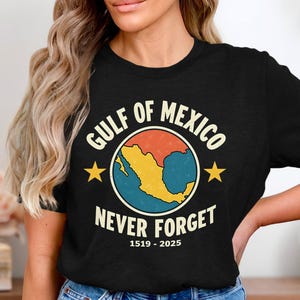 Könnte beinhalten: Schwarzes T-Shirt mit einem Grafikdesign im Vintage-Stil. Das Design zeigt einen Globus mit dem Golf von Mexiko, den Text "GULF OF MEXICO NEVER FORGET 1519-2025" und zwei gelbe Sterne. Das T-Shirt hat einen Rundhalsausschnitt.