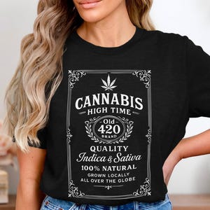 Könnte beinhalten: Schwarzes T-Shirt mit weißem Grafikdesign. Das Design zeigt das Wort "CANNABIS" über "HIGH TIME" und "Old 420 BRAND". Darunter steht "QUALITY Indica & Sativa" und "100% NATURAL".