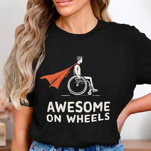 May include: Black t-shirt with a graphic of a person in a wheelchair wearing a red cape and the text "AWESOME ON WHEELS".