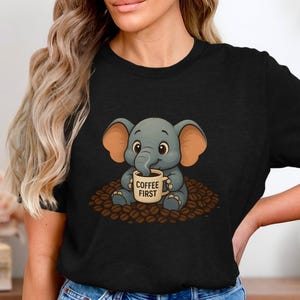 Könnte beinhalten: Schwarzes T-Shirt mit einem Cartoon-Elefanten, der eine Kaffeetasse hält. Der graue Elefant sitzt auf Kaffeebohnen. Auf der Tasse steht "COFFEE FIRST". Ein einfaches und niedliches Design.