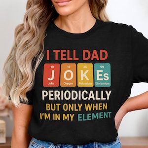 Könnte beinhalten: Schwarzes T-Shirt mit dem Text "I TELL DAD JOKES PERIODICALLY BUT ONLY WHEN I'M IN MY ELEMENT." Das Wort "JOKES" wird als Periodensystem mit den Elementen Joke, Oxygen, Potassium und Einsteinium angezeigt.