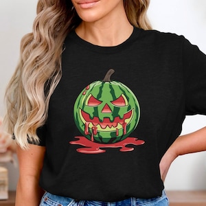 May include: A black t-shirt with a graphic of a watermelon carved into a jack-o'-lantern with dripping red blood. The watermelon has a scary face with a wide grin and sharp teeth.