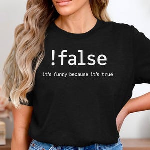 Könnte beinhalten: Schwarzes T-Shirt mit dem weißen Text "!false it's funny because it's true". Das T-Shirt hat einen Rundhalsausschnitt und wird von einer Person getragen.