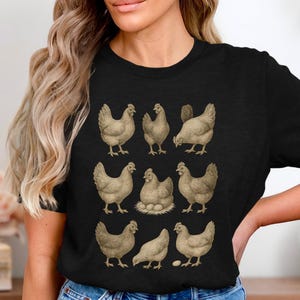 Könnte beinhalten: Schwarzes T-Shirt mit einer Vintage-Illustration von neun Hühnern in verschiedenen Posen. Die Hühner sind in Braun- und Beigetönen gehalten, mit einem Huhn auf einem Nest mit Eiern. Das Design ist auf schwarzem Hintergrund gedruckt.