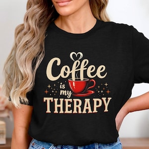 Könnte beinhalten: Schwarzes T-Shirt mit einem weißen Aufdruck, auf dem "Coffee is my therapy" steht, mit einer roten Kaffeetasse und Dampf, der aus ihr aufsteigt.