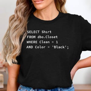 以下が含まれることがあります： 白文字で「SELECT Shirt FROM dbo.Closet WHERE Clean = 1 AND Color = 'Black';」と書かれた黒いTシャツ。クルーネックのスタイルです。