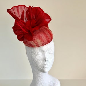 Può includere: Un cappello a righe rosse e bianche con un grande fiore rosso in cima. Il cappello è fatto di un materiale morbido e delicato ed è perfetto per un'occasione speciale.