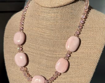 Pode incluir: Um colar com cinco contas ovais lisas em rosa pálido intercaladas com contas de cristal mais pequenas e facetadas em rosa claro. O design alterna entre os elementos ovais maiores e de cor sólida e os componentes de cristal refletores.