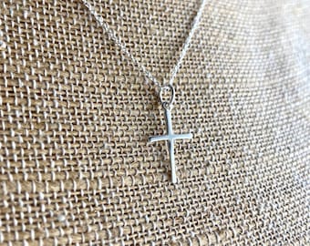 May include: A silver chain necklace with a simple silver cross pendant.