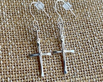 May include: A pair of silver dangle earrings with a cross charm. The cross is textured and has a rustic look.