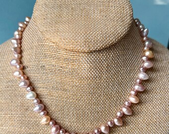 Pode incluir: Um colar composto por numerosas pérolas de água doce irregulares, em forma de gota e redondas, em tons variados de rosa suave, lavanda e creme. As pérolas estão enfiadas num único fio, exibindo um brilho natural e tamanhos variados.