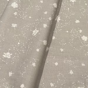 May include: A close-up of a gray fabric with a white dandelion print. The fabric has a subtle texture and the dandelions are scattered throughout the fabric. The text "Dancing Daisies" is visible at the bottom of the image.