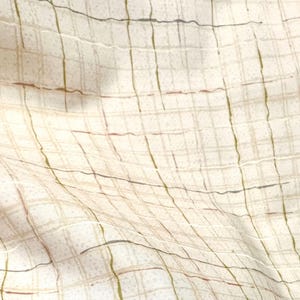 May include: Close-up of a cream-colored fabric with a grid pattern. The grid is formed by thin, irregular lines in shades of brown, green, and gray. The fabric has a slightly textured appearance, with subtle variations in color and tone.