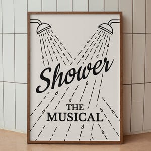 Puede incluir: Una impresión artística enmarcada con fondo blanco presenta dos alcachofas de ducha con gotas de agua. El texto negro dice "Shower" encima de "The Musical". El marco es de color marrón cálido.