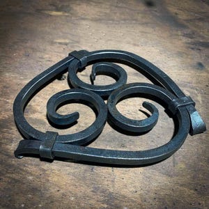 May include: A black metal trivet with a heart shape and three decorative swirls.