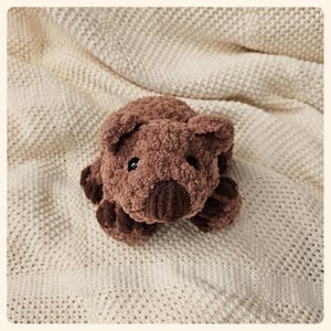 May include: A brown plush toy shaped like a wombat, lying on a white knitted blanket.