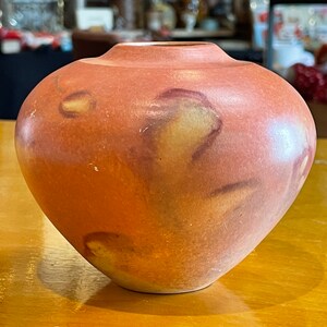 May include: A small, round, terracotta vase with a mottled orange and brown glaze. The vase has a slightly flared lip and a rounded bottom.