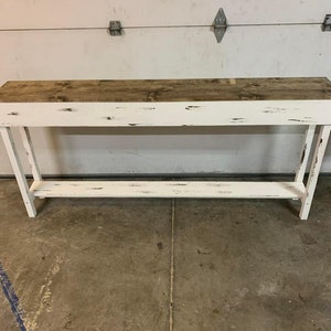 May include: White distressed wood console table with a single shelf. The table has a rustic, farmhouse style.