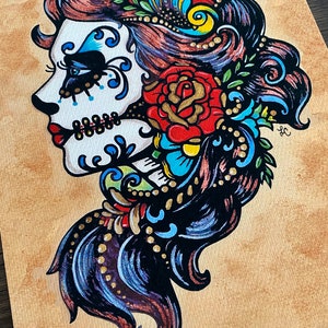 May include: A colorful illustration of a Day of the Dead sugar skull woman with a red rose and floral details. The skull is painted in white with blue and black accents. The woman's hair is black with blue and gold highlights. The background is a light brown.