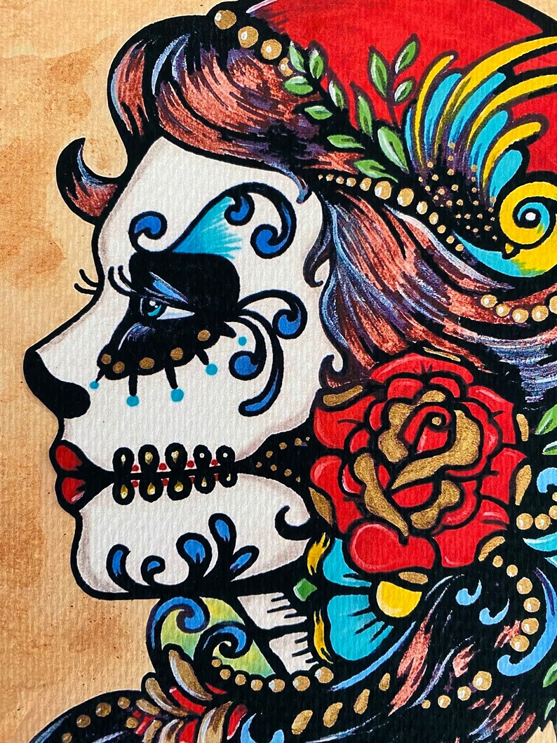 May include: A colorful illustration of a woman with a sugar skull face, red lips, and a red rose. The woman is wearing a red head scarf with gold beads and a blue and yellow feather. The background is a light brown.