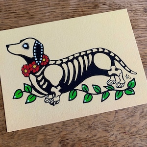 May include: A black and white illustration of a dachshund skeleton with red and white flowers around its neck. The dachshund is walking on a green vine with white flowers.