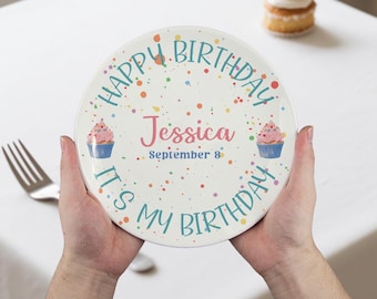 Puede incluir: Un plato de cumpleaños personalizado con el texto "Happy Birthday, It's My Birthday" en color turquesa. El plato está decorado con confeti colorido y dos ilustraciones de cupcakes. El nombre "Jessica" y la fecha "September 8" también aparecen.