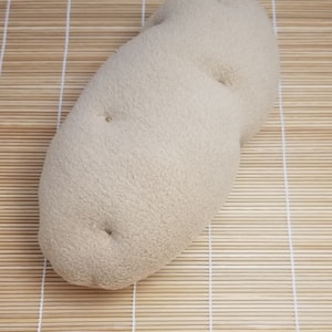 May include: A plush, beige potato-shaped pillow. The pillow is soft and fluffy, with a slightly bumpy texture.