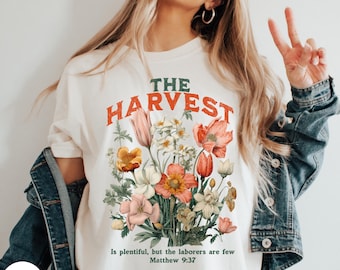 Puede incluir: Camiseta blanca con un diseño floral y el texto "THE HARVEST is plentiful, but the laborers are few Matthew 9:37".