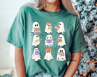 May include: A light green t-shirt with a graphic of nine ghosts reading books. The ghosts are white and have different poses, some holding books, some with stacks of books, and some with books on their heads.