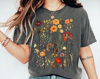 Może przedstawiać: Szary T-shirt z nadrukiem kwiatowym przedstawiającym różne kwiaty i liście w odcieniach czerwieni, pomarańczy, żółci i zieleni.