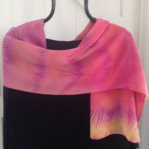 May include: A pink and yellow silk scarf with a geometric pattern, draped over a black dress.