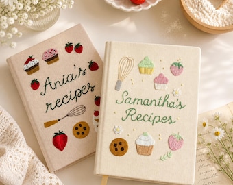 Puede incluir: Dos cuadernos de recetas beige con diseños bordados. Uno dice "Ania's recipes" y el otro "Samantha's Recipes". Ambos presentan bordados de cupcakes, fresas y otras imágenes relacionadas con la repostería.