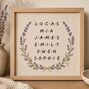 Könnte beinhalten: Ein quadratischer Holzrahmen mit einem Stoff, auf dem die Namen LUCAS, MIA, JAMES, EMILY, OWEN und SOPHIE handgestickt sind. Jeder Buchstabe ist durch einen kleinen farbigen Punkt getrennt. Ein Kranz aus Lavendelzweigen und weißen Gänseblümchen umrahmt die Namen.