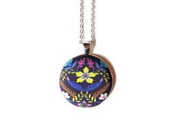 Puede incluir: Un collar de cadena plateada con un colgante redondo que presenta un patrón floral sobre un fondo negro. El colgante tiene flores amarillas, rosas, azules y naranjas.
