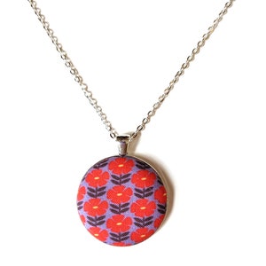 The fabric pendant necklace is hanging from a silver colored chain. The pendant has a light purple background with a pattern of red flowers.